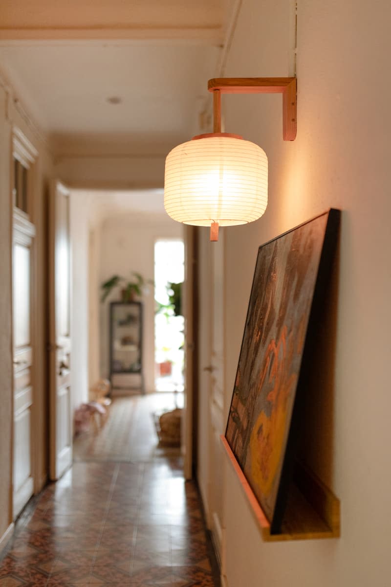 Paper lantern sconce lights artwork in neutral hallway.