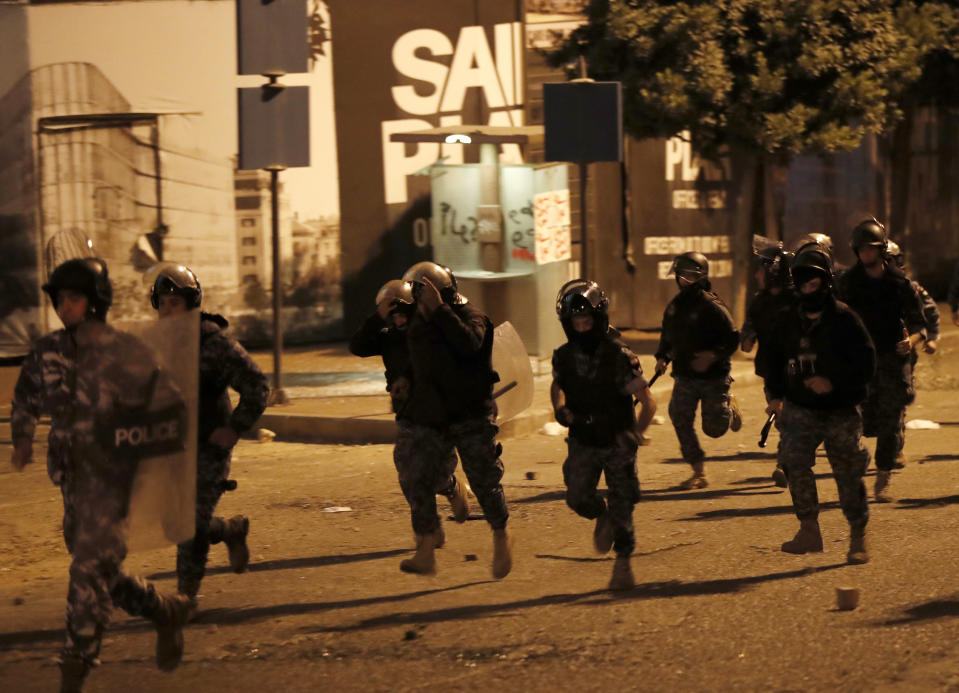 Lebanese riot policemen run after a clash erupted between the supporters of the Shiite Hezbollah and Amal Movement groups and the anti-government protesters, in Beirut, Lebanon, early Monday, Nov. 25, 2019. Security forces fired tear gas amid confrontations in central Beirut that went into Monday morning between Hezbollah supporters and demonstrators protesting against Lebanon's political elite. (AP Photo/Hussein Malla)