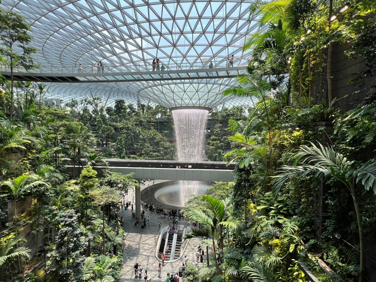 glass circular building with 280 restaurants and stores and a 40-meter-high circular indoor waterfall. It is surrounded by hanging terraced gardens at the airport in Singapore