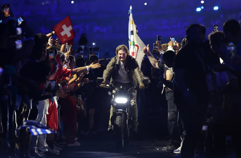  Tom Cruise, without a helmet, rides a motorbike flying the IOC flag through a crowd during the closing ceremony.