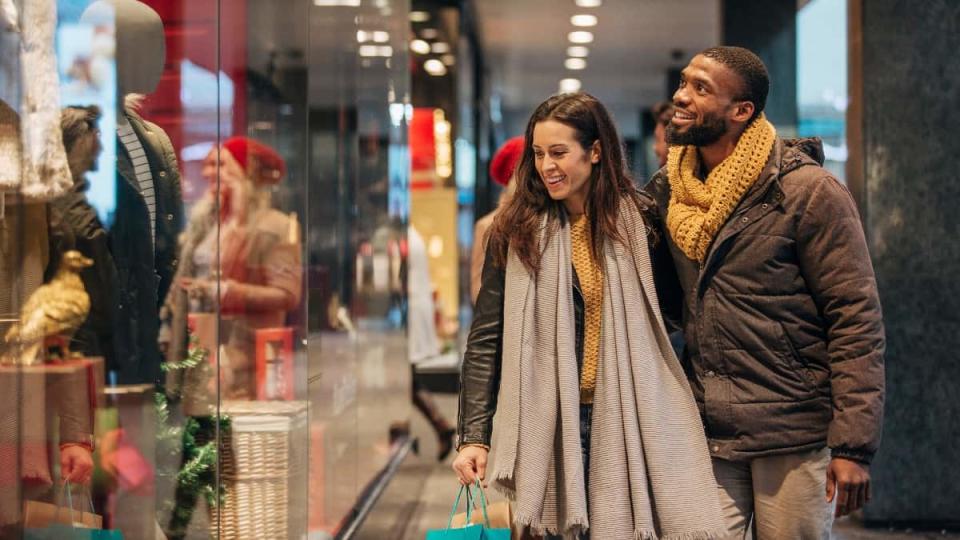 Front view of an interracial couple walking past a store window and looking inside.