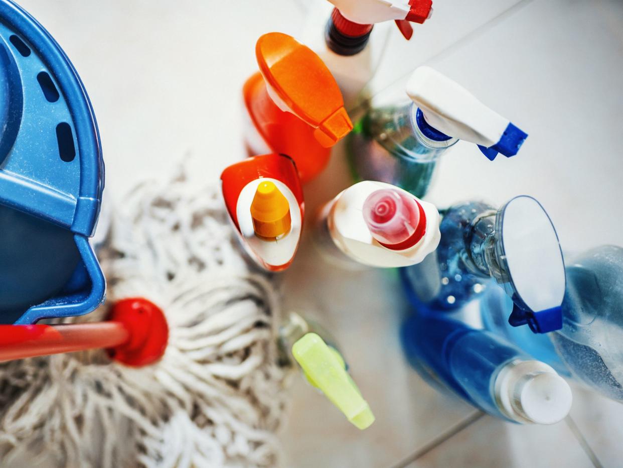 Closeup top view of unrecognizable home cleaning products with blue bucket and a mop on the side. All products placed on white tiled bathroom floor.