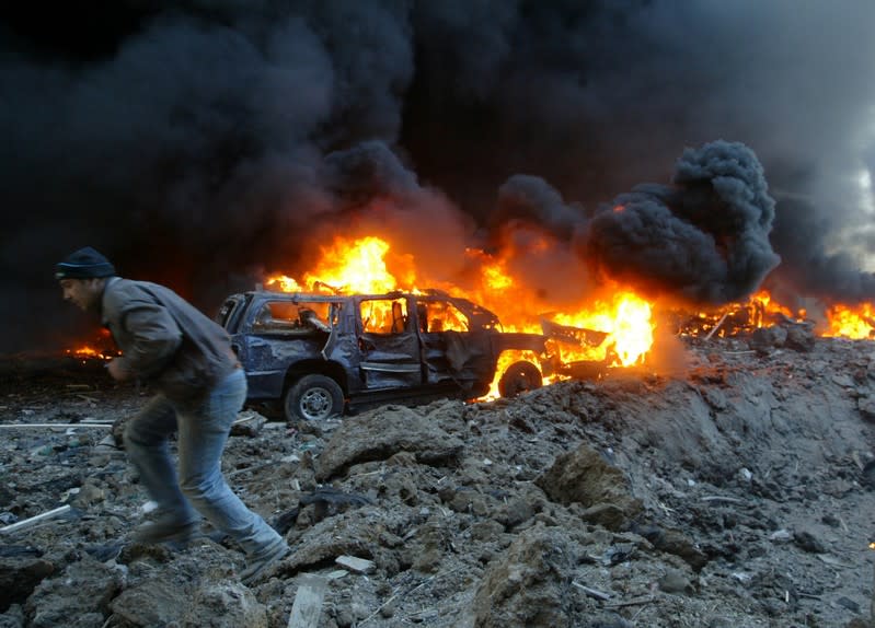 FOTO DE ARCHIVO: Un hombre libanés pasa junto al convoy en llamas del ex primer ministro Rafik al-Hariri en Beirut el 14 de febrero de 2005