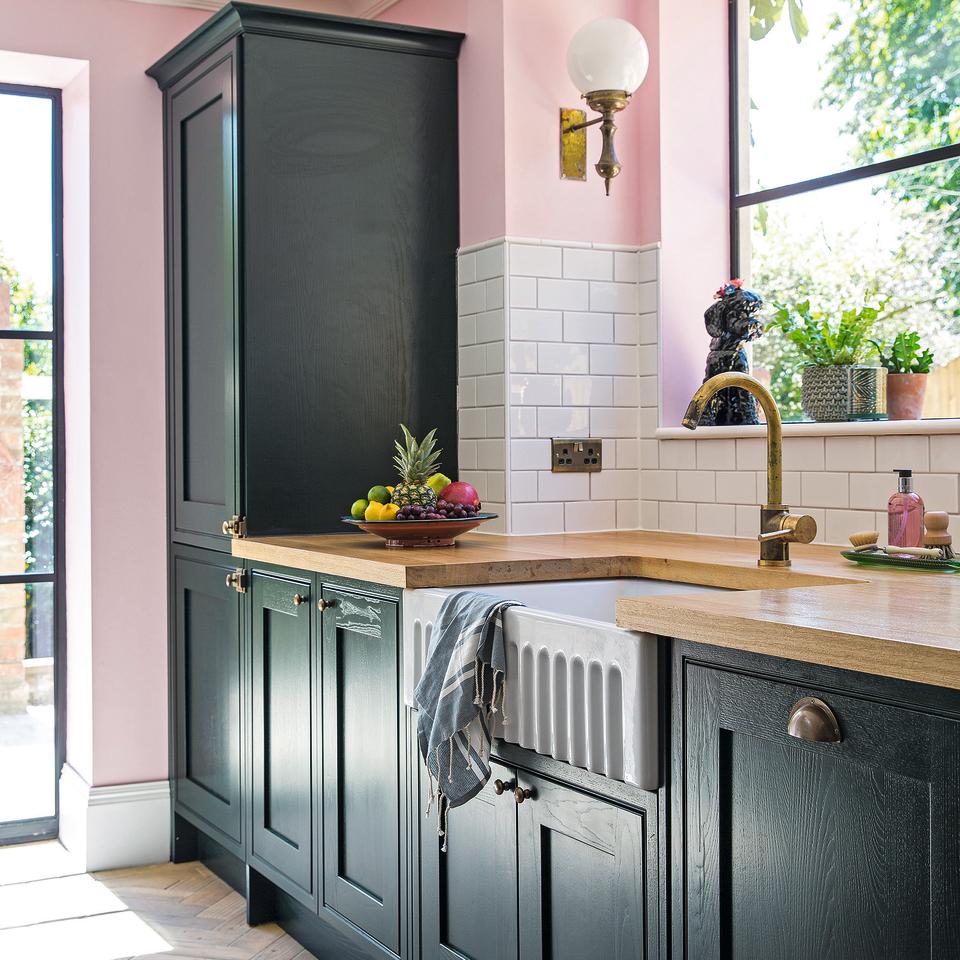 Dark green shaker kitchen with grained cupboards and pink walls.