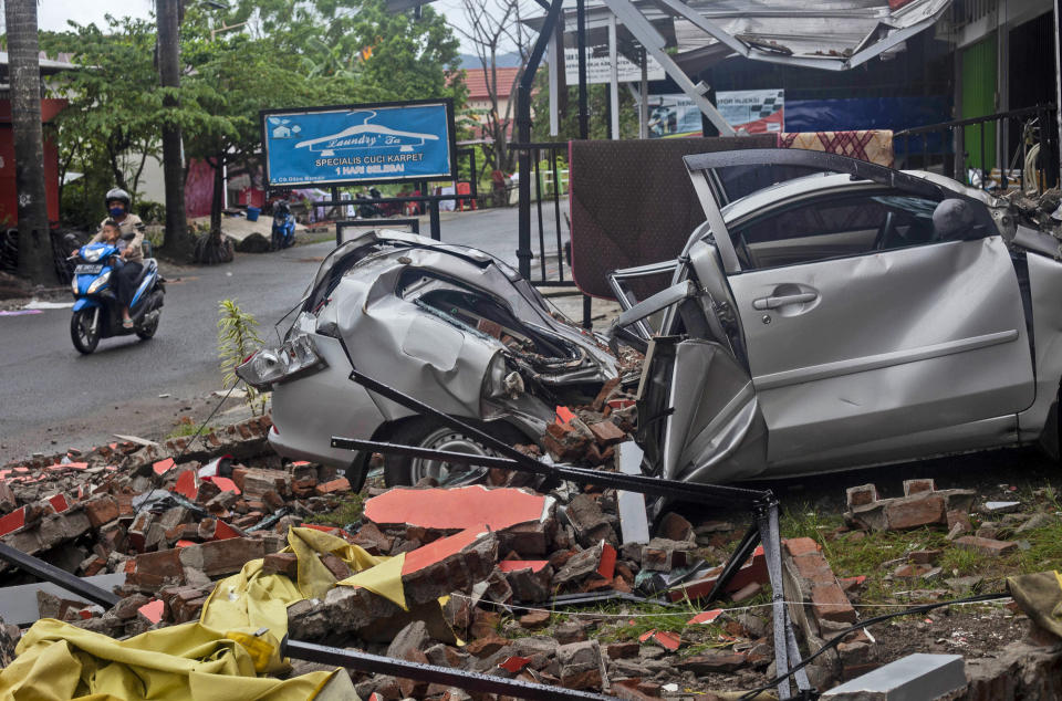 A motorist rides past the wreckage of a car damaged in an earthquake in Mamuju, West Sulawesi, Indonesia, Saturday, Jan. 16, 2021. Damaged roads and bridges, power blackouts and lack of heavy equipment on Saturday hampered Indonesia's rescuers after a strong and shallow earthquake left a number of people dead and injured on Sulawesi island. (AP Photo/Yusuf Wahil)