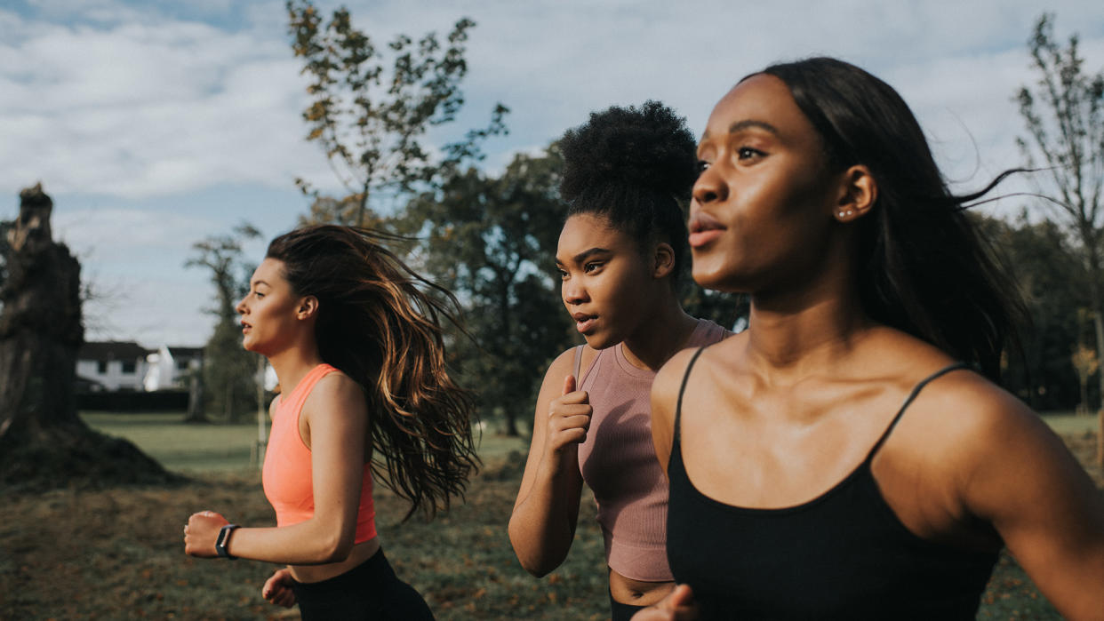  Strong, fit woman joggers, running through a sunny park at sunrise. They look determined as they put in the effort. Their hair blows behind them as they look in front of them. . 