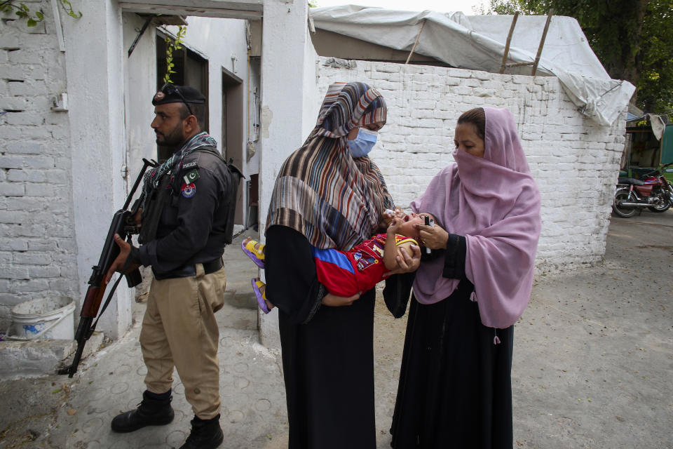 A police officer stands guard as a health worker, right, administers a polio vaccine to a child in a neighbourhood of Peshawar, Pakistan, Monday, Sept. 9, 2024. (AP Photo/Muhammad Sajjad)