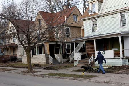 A man walks a dog past a row of vacant houses on Crandall Street, a street that became a hub for narcotics activity according to local media and police, in Binghamton, New York, U.S., April 8, 2018. REUTERS/Andrew Kelly