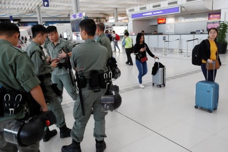 Passengers walk past riot police standing inside Hong Kong International Airport in Hong Kong, China