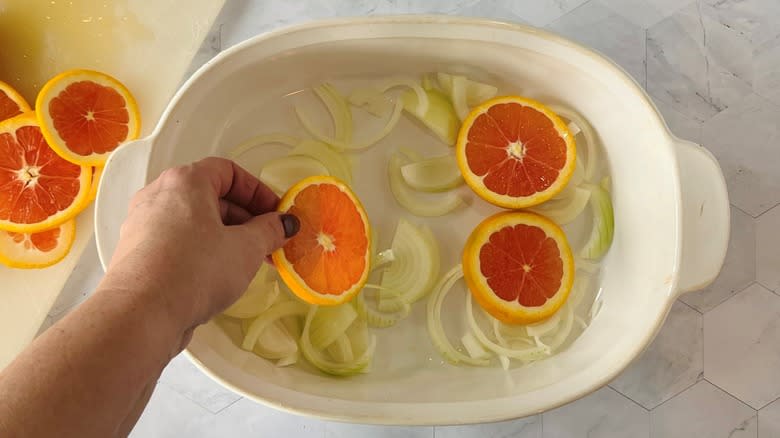 arranging orange slices in dish over onions