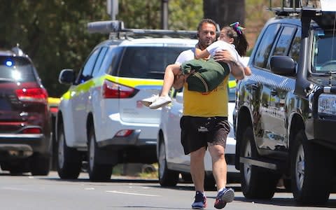 A man carries a child near where a vehicle crashed into a primary school classroom in the Sydney suburb of Greenacre - Credit: Reuters