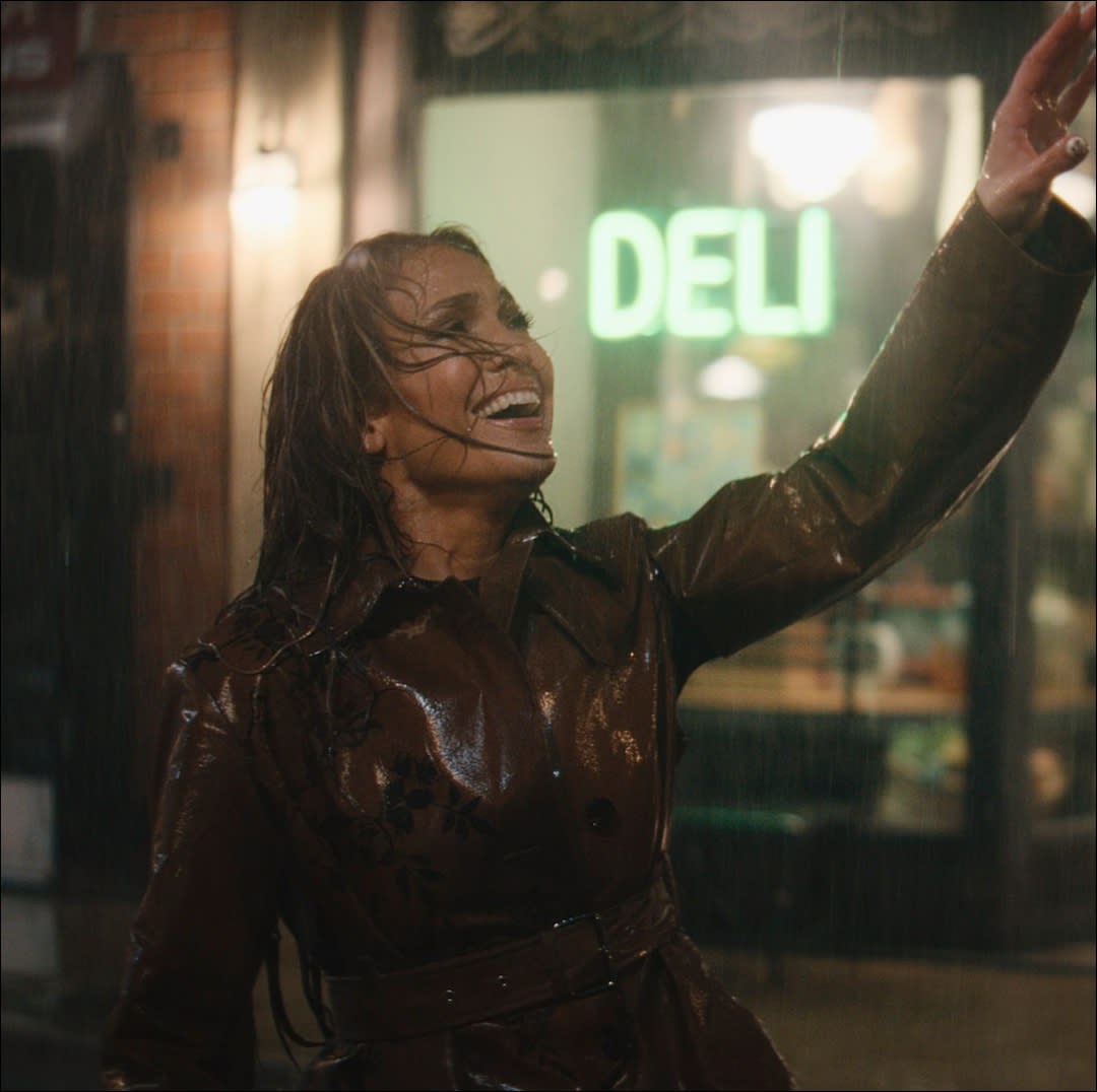  A woman (jennifer lopez) raises her hand while singing in the rain. 