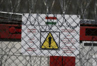 A warning sign is attached to a fence at Serbia's border with Hungary near a makeshift camp for migrants in Horgos, Serbia, Tuesday, March 28, 2017. Hungary's new legislation allowing for the placement of all asylum-seekers in border container camps took effect Tuesday, with the European Union's commissioner for migration saying that it needs to comply with the bloc's rules. (AP Photo/Darko Vojinovic)