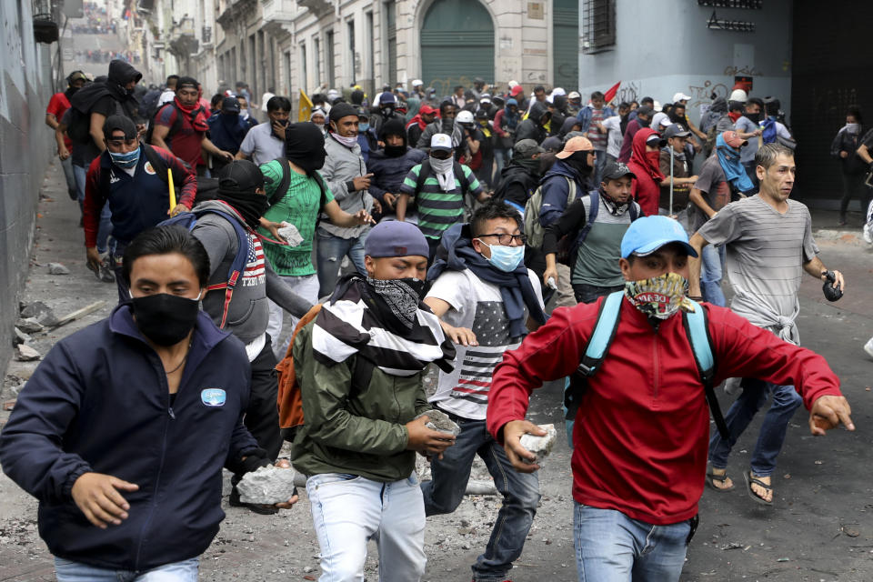 Anti-government protesters, stones in hand, run during clashes in downtown Quito, Ecuador, Wednesday, Oct. 9, 2019. Ecuador's military has warned people who plan to participate in a national strike over fuel price hikes to avoid acts of violence. The military says it will enforce the law during the planned strike Wednesday, following days of unrest that led President Lenin Moreno to move government operations from Quito to the port of Guayaquil. (AP Photo/Fernando Vergara)