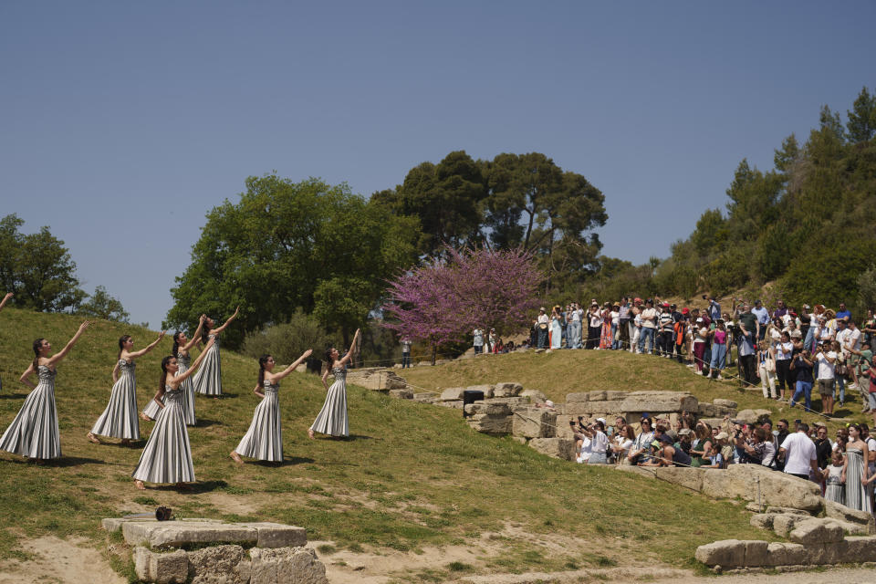 Visitors watch the performers, who will take part in the flame lighting ceremony for the Paris Olympics, during a rehearsal at Ancient Olympia site, Greece, Sunday, April 14, 2024. Every two years, a countdown to the Olympic games is launched from its ancient birthplace with a flame lighting ceremony in southern Greece at Ancient Olympia. The event is marked with a performance by dancers who assume the role of priestesses and male companions, their movement inspired by scenes on millennia-old artwork. (AP Photo/Petros Giannakouris)