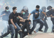 Amid tear gas clouds, plain-clothed police officers detain protesters during a rally in Jakarta, Indonesia, Thursday, Oct. 8, 2020. Thousands of enraged students and workers staged rallies across Indonesia on Thursday in opposition to a new law they say will cripple labor rights and harm the environment.(AP Photo/Tatan Syuflana)