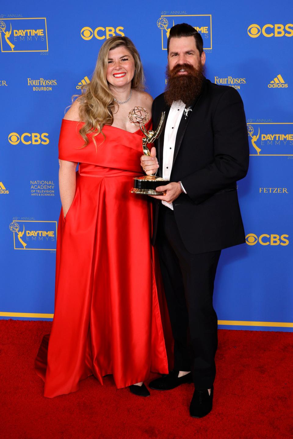 Candis and Andy Meredith pose on a red carpet with an Emmy award.