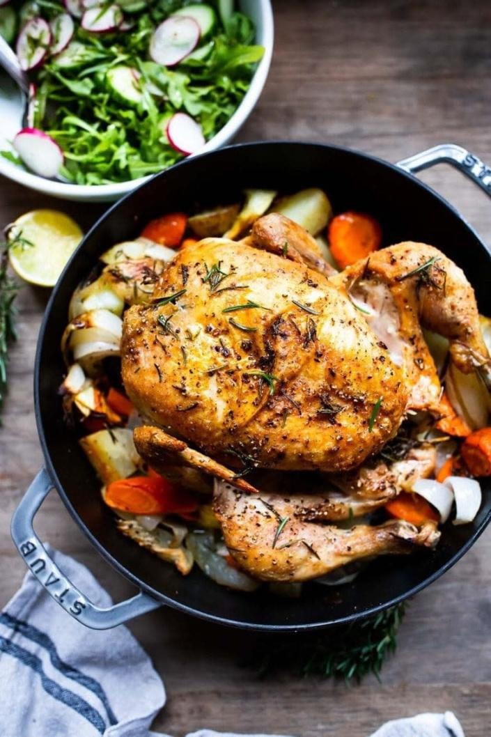 A whole roast chicken and vegetables in a skillet.