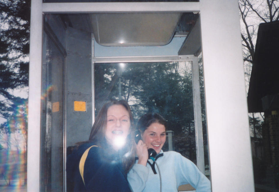 Two young women smiling while inside a phone booth; the mood appears candid and joyful