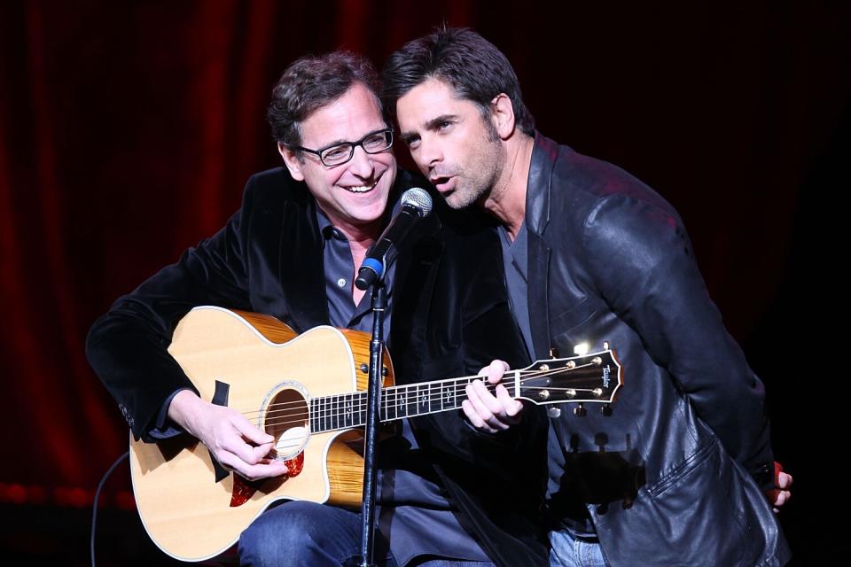 Bob Saget with a guitar and John Stamos singing into a microphone