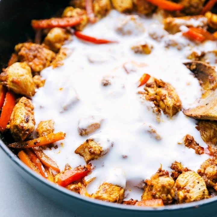 Coconut milk on top of chicken and peppers in a skillet
