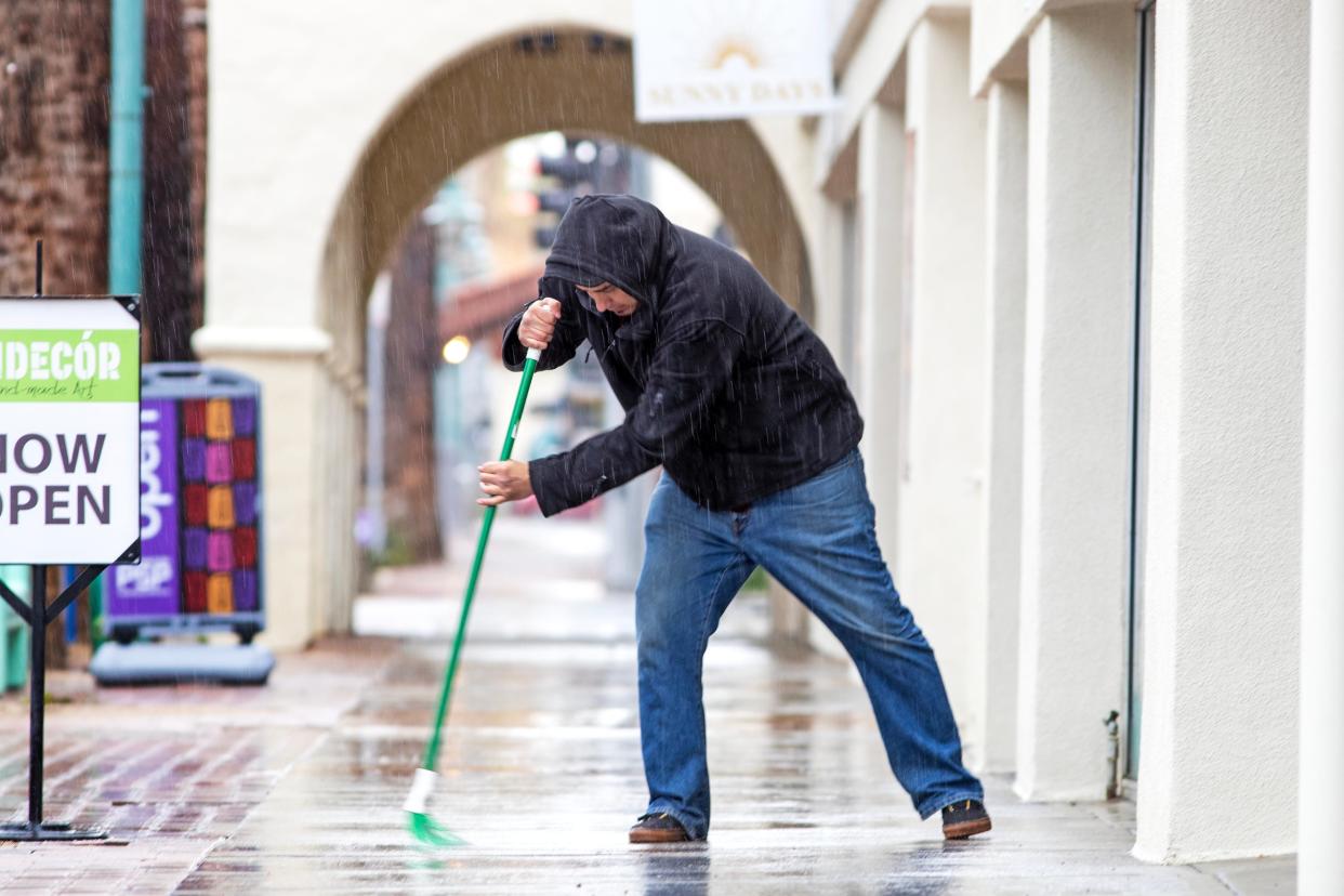 Calvin Cardenas sweeps the sidewalk outside Andecor as rain falls in Palm Springs on March 1.