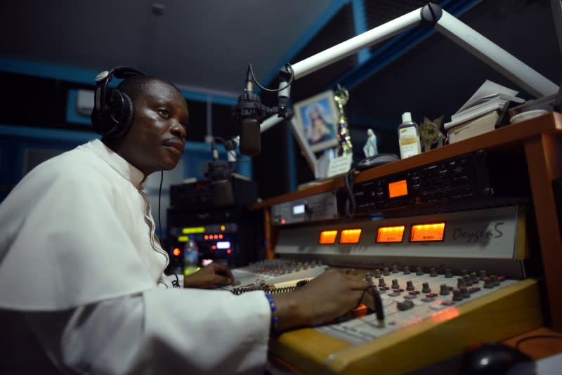 Reverend Father John Peter Bebeley sits behind the mixing table at Radio Maria, in Freetown