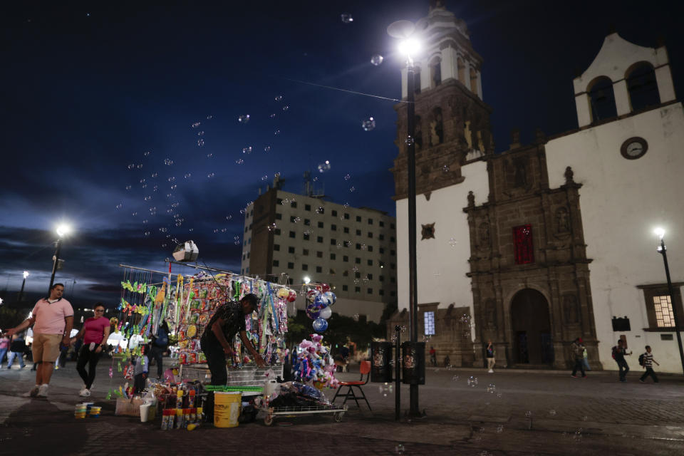 In this Feb. 12, 2020 photo, people and vendors mingle on a central plaza as night falls, in Irapuato, Guanajuato state, Mexico. The state is attractive to drug cartels for the same reason it is to auto manufacturers: road and rail networks that lead straight to the U.S. border. (AP Photo/Rebecca Blackwell)