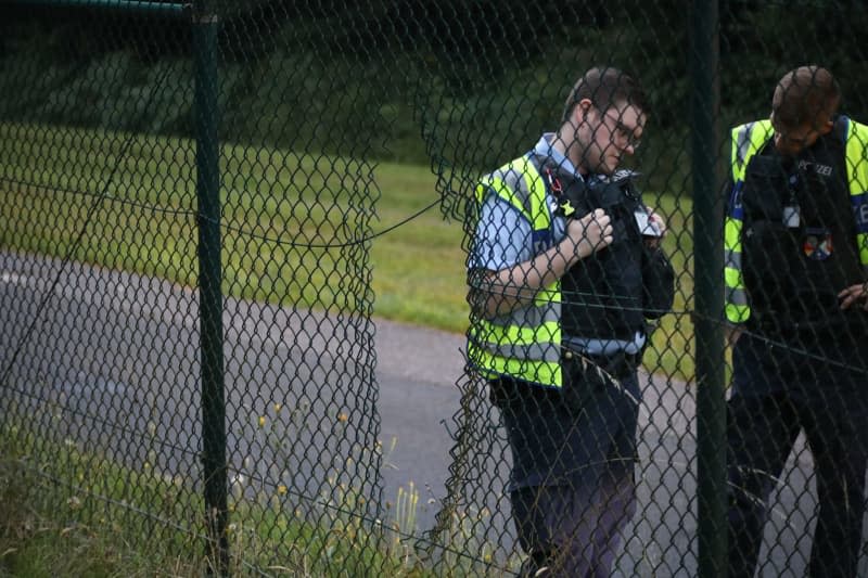 Police officers stand next to a hole in the fence at Cologne/Bonn Airport. Five climate activists have glued themselves to the apron at Germany's Cologne/Bonn airport, causing air traffic to be suspended. Uncredited/dpa