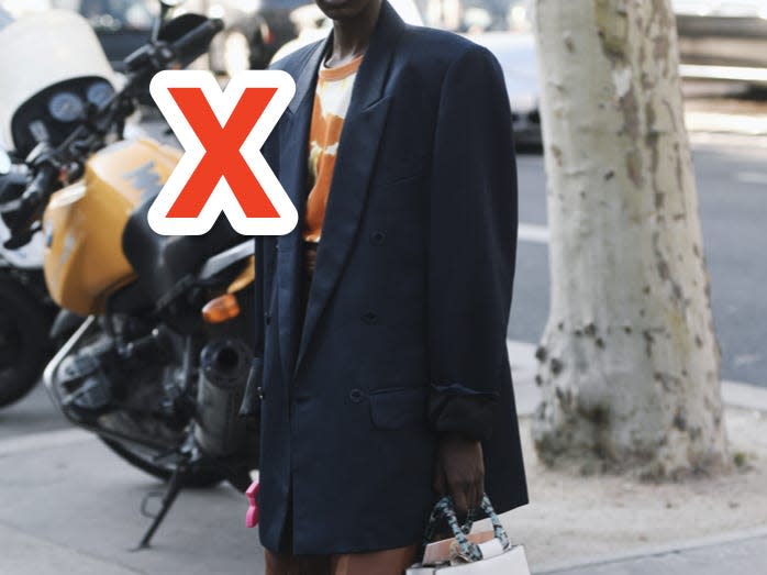 red x over someone's black oversized blazer as they pose for a photo in a street