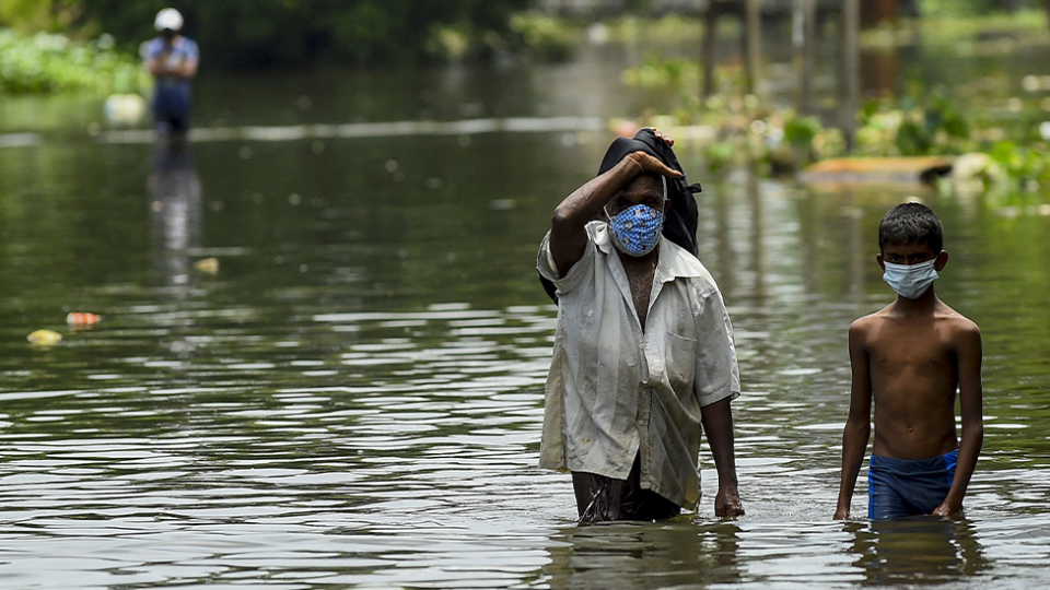 A man and a boy walking down a flooded street in Sri Lanka in 2021. Extreme weather events are linked to climate change.  