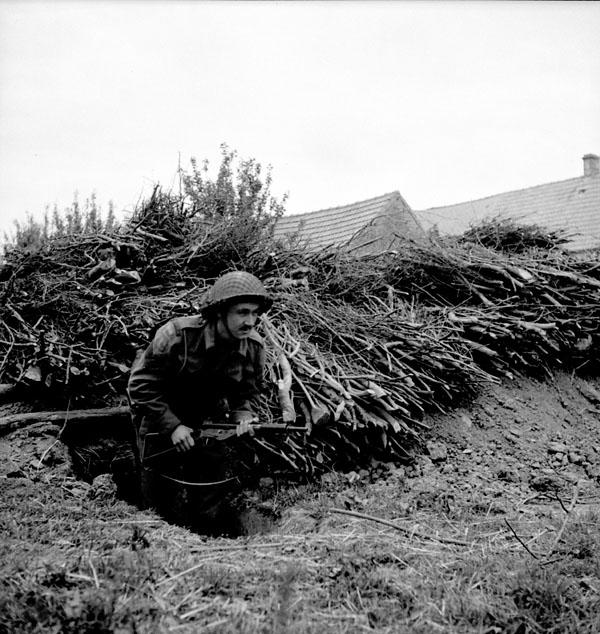 An unidentified Canadian infantryman standing guard in a dugout outside No. 3 Canadian Public Relations Group (Canadian Army Miscellaneous Units) headquarters in the Normandy beachhead, France, June 9, 1944.