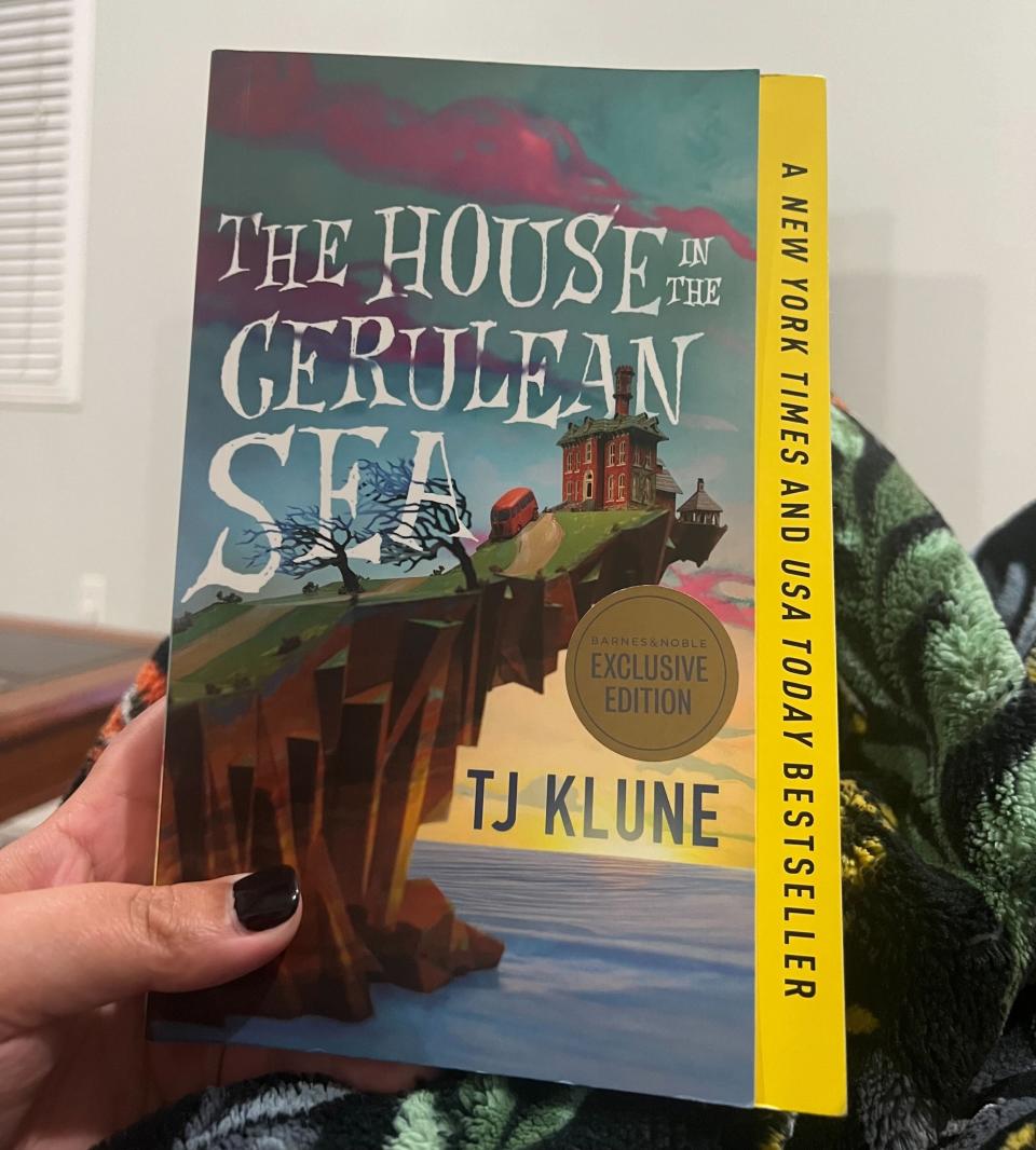 The author is holding a copy of "The House in the Cerulean Sea" by TJ Klune