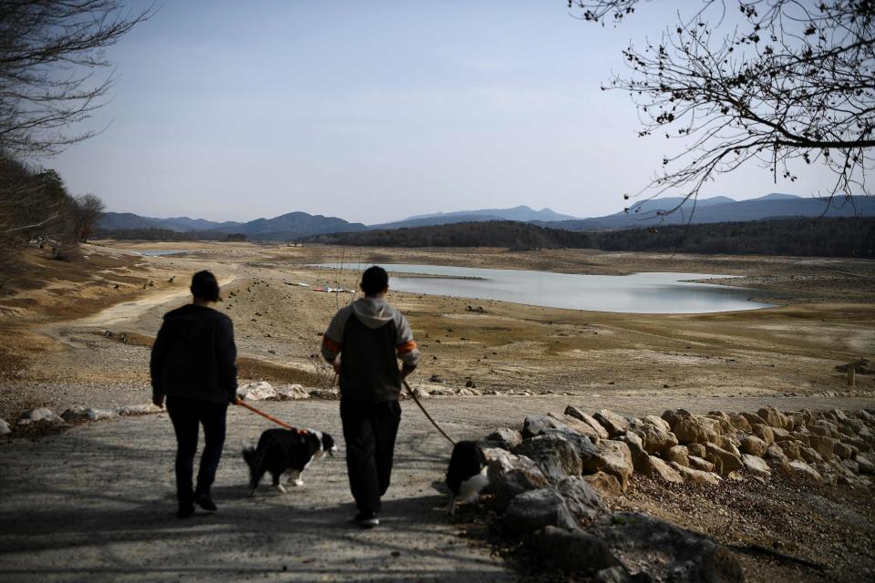 Two people walk their dogs near the partially dry Lake Montbel, south-western France, on February 21, 2023.