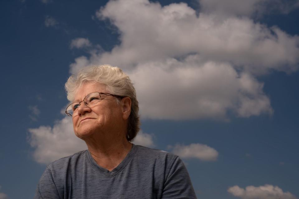 A smiling woman with glasses in three-quarter profile against a cloudy sky