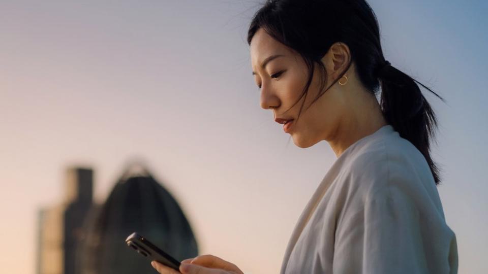 Una mujer mira su teléfono al atardecer.