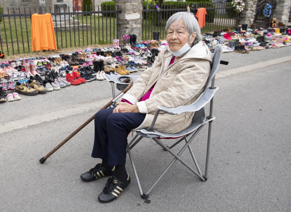 Residential school survivor Betty Deer sits next to children's shoes, placed there as a tribute to the victims of the residential school system outside St. Francis Xavier Church in Kahnawake, Quebec, Sunday, May 30, 2021. The remains of 215 children, some as young as 3 years old, have been found buried on the site of what was once Canada's largest Indigenous residential school — one of the institutions that held children taken from families across the nation. (Graham Hughes/The Canadian Press via AP)