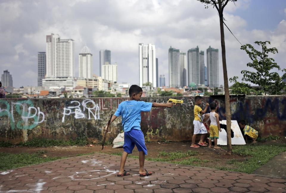 In this Monday, Feb. 13, 2017 photo, a boy plays with a toy gun as the city skyline is seen in the background in Jakarta, Indonesia. Residents of Indonesia's capital vote Wednesday in an election for governor that has become a high-stakes tussle between conservative and moderate forces in the world's most populous Muslim nation. Religion and race, rather than the slew of problems that face a car-clogged and sinking Jakarta, have dominated the campaign. (AP Photo/Dita Alangkara)