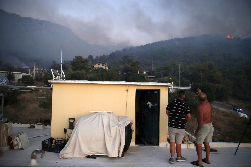 A local resident, right, speaks to a reporter on the wildfire in Peania, eastern Athens, Monday, Aug. 12, 2019. A big fire broke out in the Athens suburb of Peania east of the city, and authorities ordered the evacuation of nearby houses. (AP Photo/Thanassis Stavrakis)
