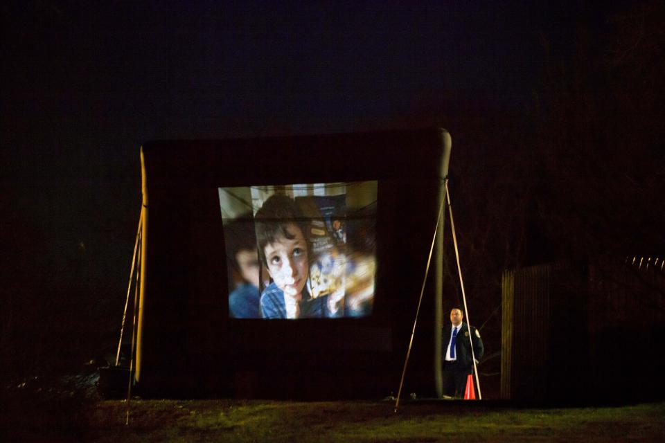 FILE - An image of 6-year-old Sandy Hook Elementary School shooting victim Benjamin Andrew Wheeler is projected on a big screen behind the Trinity Episcopal Church as a mourner, at right, looks on during his wake, Wednesday, Dec. 19, 2012, in Newtown, Conn. Wheeler’s father, David, recalled learning of the Colorado theater shooting that preceded Sandy Hook and claimed the life of Jessica Ghawi, the daughter of Sandy Phillips. At the time, he paused just for a moment to think of the families who had lost someone, “Oh my God, those poor people.” Now, two of those people, Sandy and her husband, Lonnie, were before him, and he was living through the same. (AP Photo/David Goldman, File)