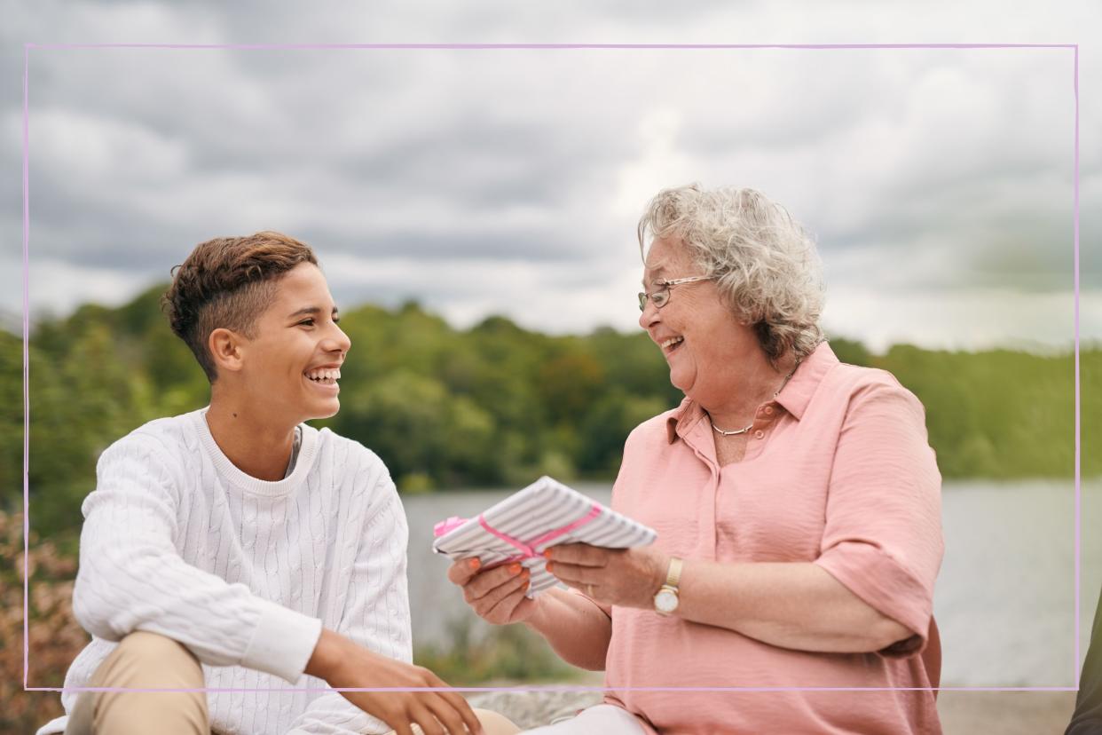  A grandmother and teenage boy laughing together while sitting outside. 