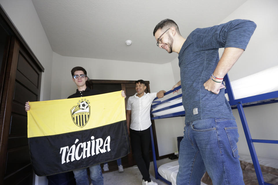 Cesar Baez, left, holds a soccer club flag from his home state of Táchira in Venezuela, as Jenderson Rondon, center, and Henry Nadales look on, at the house of Dr. Kyle Varner, who is their program sponsor, Friday, Jan. 6, 2023, in Spokane, Wash. They are beneficiaries of a Venezuelan humanitarian parole program. (AP Photo/Young Kwak)