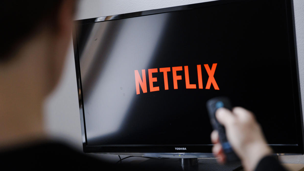  A man watches the Netflix logo on a Toshiba TV with a remote in his hand. 