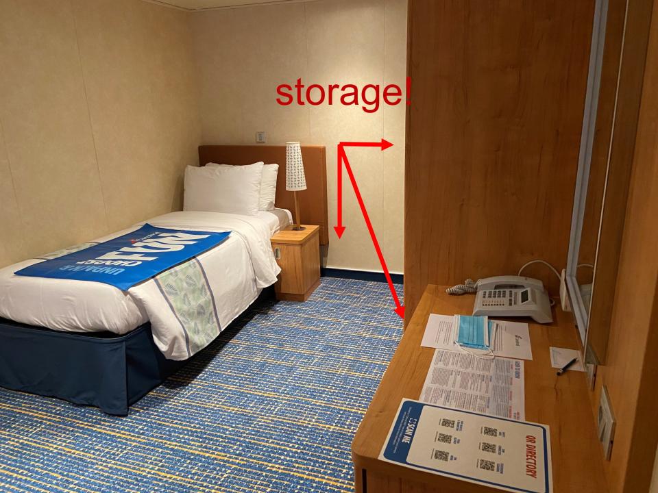 A cruise ship room with a bed and a desk and arrows pointing to places for storage.