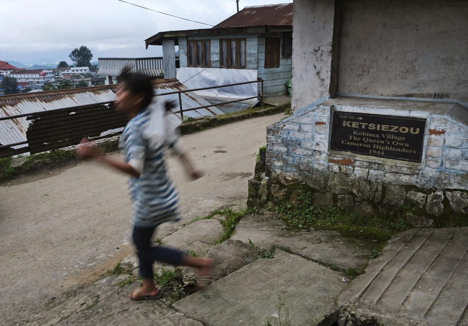 A Naga girl runs down a lane with a plaque planted by the British commemorating the Queens Own Cameron Highlanders, an infantry regiment of the British Army, in Kohima village, the site of a bloody WWII battle, India, Tuesday, Aug. 11, 2020. Between April and June 1944, Japanese and British Commonwealth forces fought across Kohima and the area around it in a battle that has been chosen as Britain's greatest battle by the National Army Museum, along with their battle in neighboring Imphal region. (AP Photo/Yirmiyan Arthur)