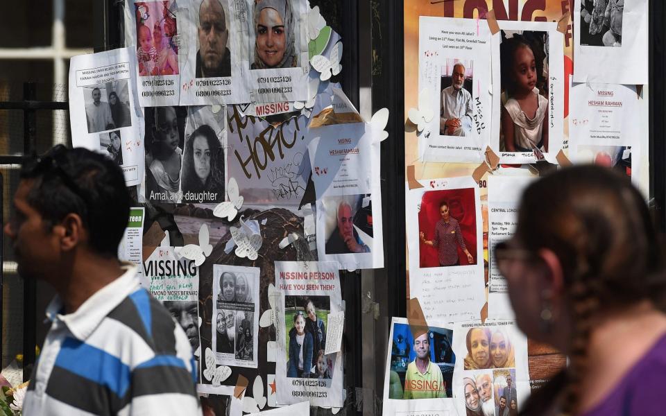 People pass posters showing images of missing people, in Kensington, west London - Credit: PAUL ELLIS/AFP/Getty Images