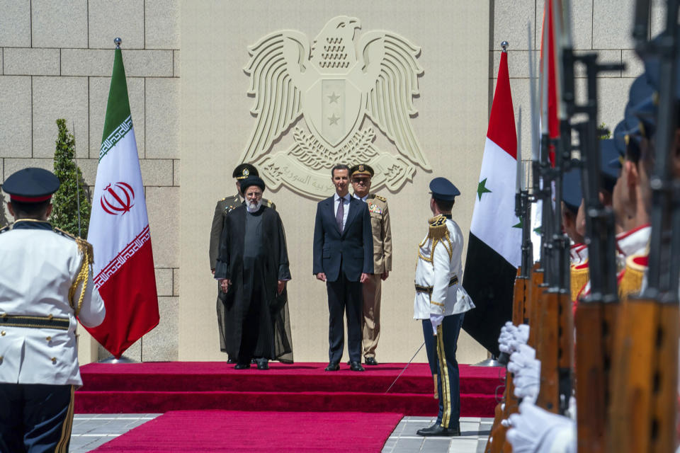 In this photo released by the official Facebook page of the Syrian Presidency, Syrian President Bashar Assad, center right, and Iranian President Ebrahim Raisi, center left, review an honor guard during a welcome ceremony upon Raisi's arrival in Damascus, Syria, Wednesday, May 3, 2023. (Syrian Presidency via Facebook via AP)