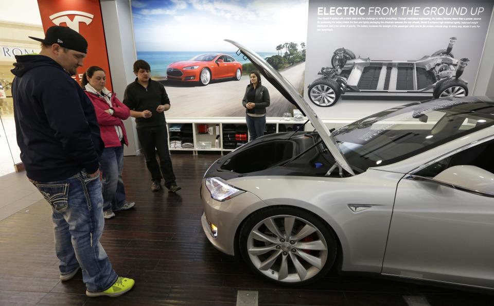 Robert and Sarah Reynolds, left, check out a new Tesla all electric car with Tesla representatives John Van Cleave and Raven Rivera, right, Monday, March 17, 2014, at a Tesla showroom inside the Kenwood Towne Centre in Cincinnati. Ohio auto dealers are sparring at the Statehouse with the California-based Tesla, which is selling it's next generation electric cars from three Ohio storefronts. Lawmakers in Ohio and other states are trying to block Tesla direct sales on grounds they undercut traditional auto dealerships. (AP Photo/Al Behrman)