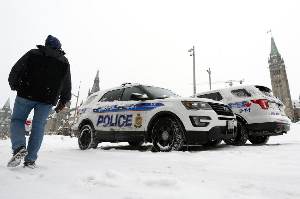 A person passes Ottawa police officers in their vehicles on Wellington Street in front of Parliament Hill as demonstrators mark one year since the start of the self-styled 'Freedom Convoy' Jan. 29, 2023.