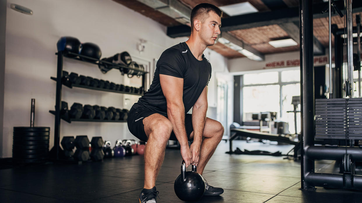  Man doing squat with kettlebell. 